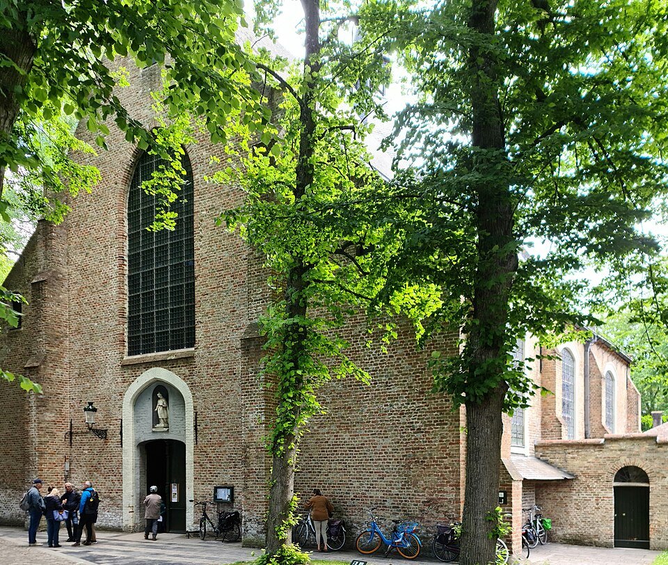 The brick front of the Beguinage church framed by trees