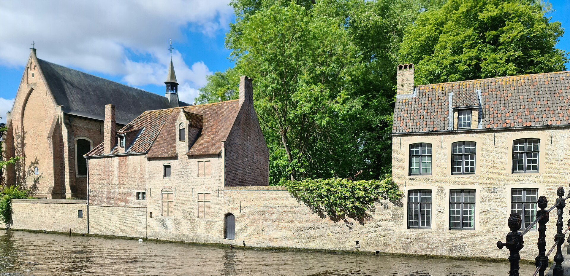 The Beguinage from the canal: brick houses, garden walls and the church roof among trees