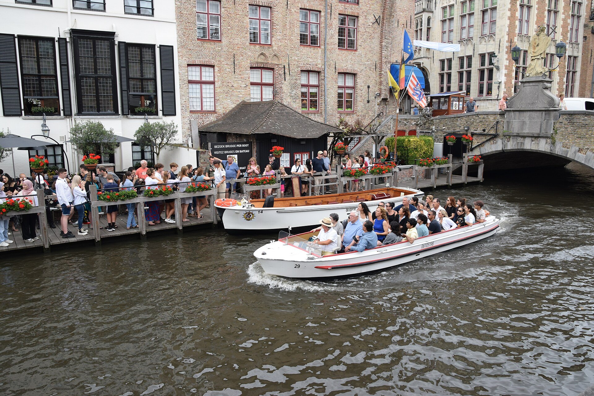 A canal boat full of passengers turning below a landing stage