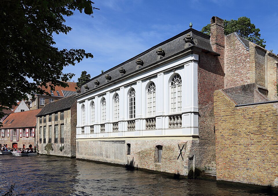 A white orangery with tall arched windows standing over the water