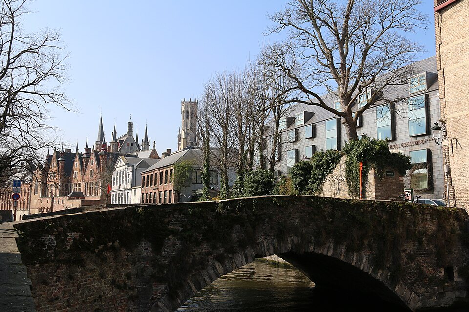 An old stone bridge in the foreground, the towers of the center beyond bare trees