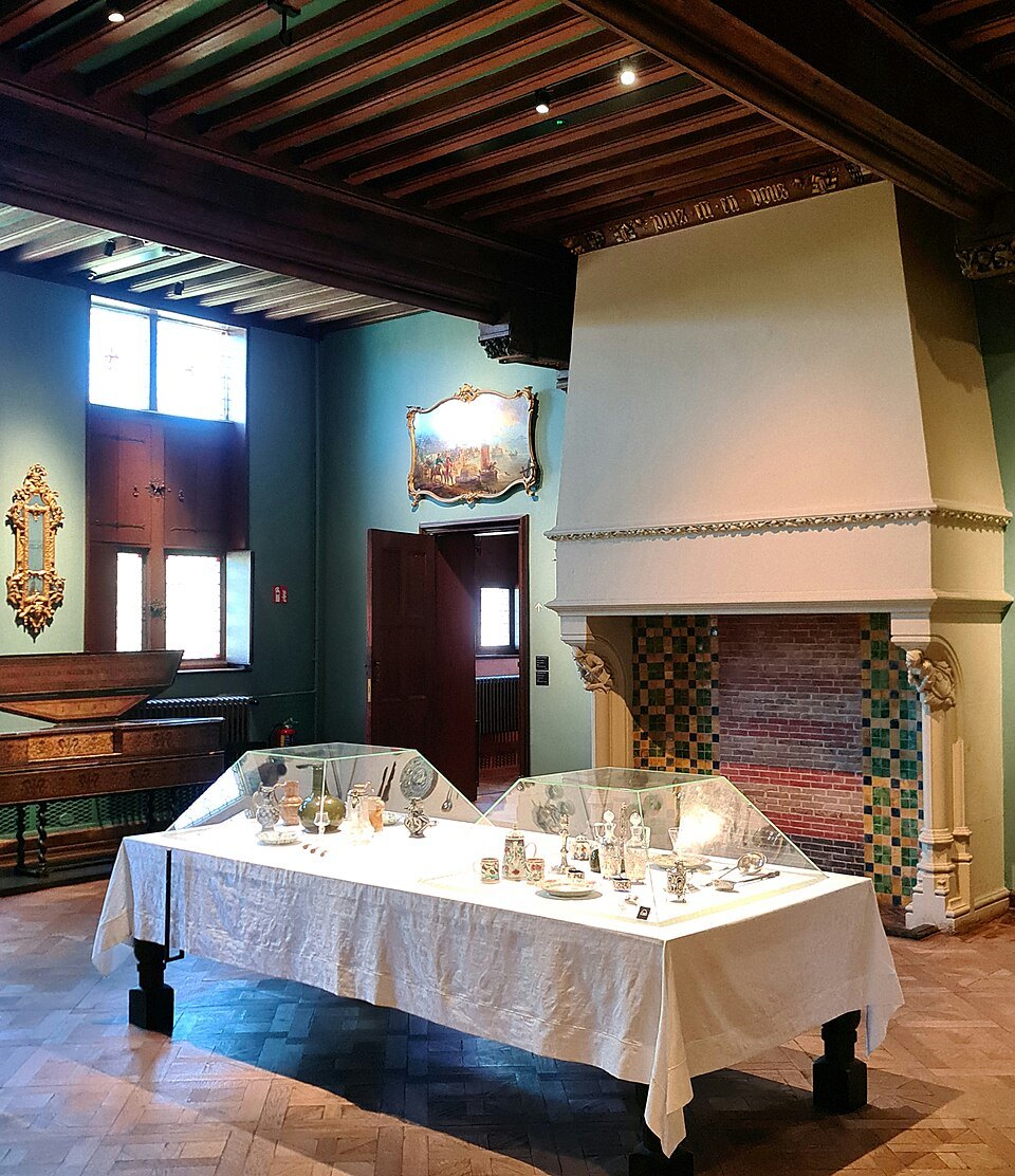 Silverware on a white-clothed table beneath a great hooded fireplace
