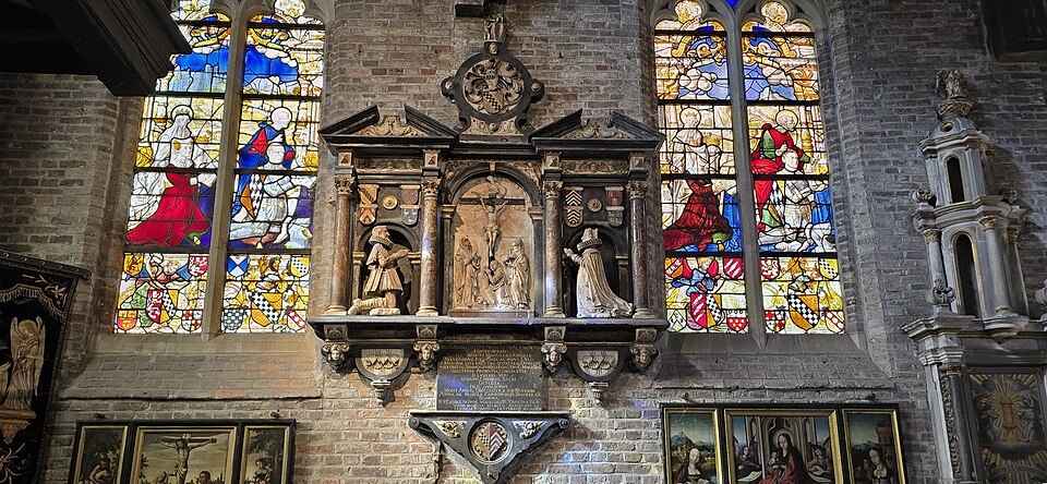 Stained-glass windows with colored figures on either side of a carved memorial