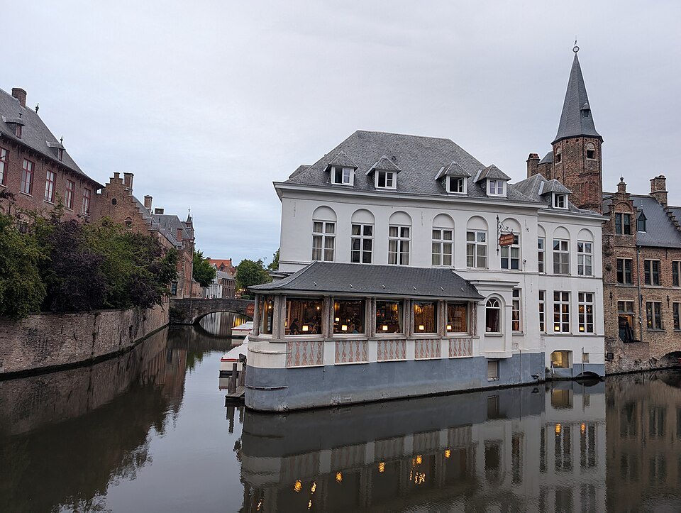 A white building with a glassed terrace reflected in the canal
